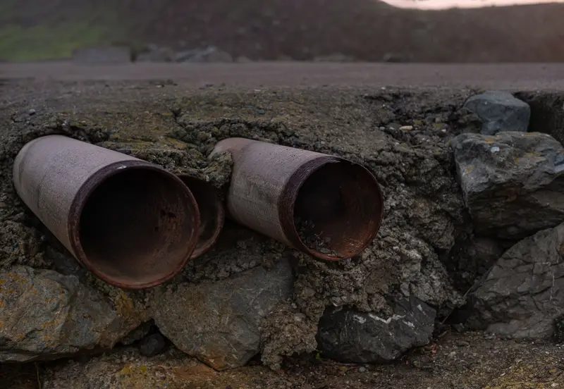 Old excavated pipe sections lying among rocks in a trench.