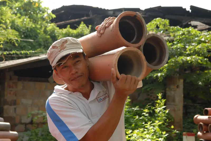 Smiling worker carrying old clay pipe sections on his shoulder.