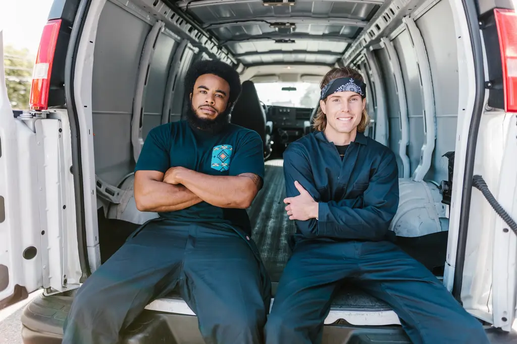 Two smiling crew members sitting in the open back of a white service van.