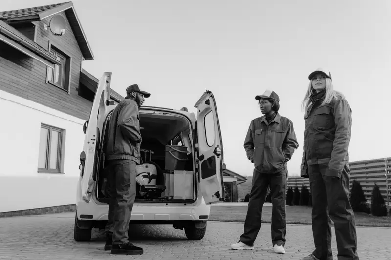 Three workers in work clothes talking beside an open van, black and white.