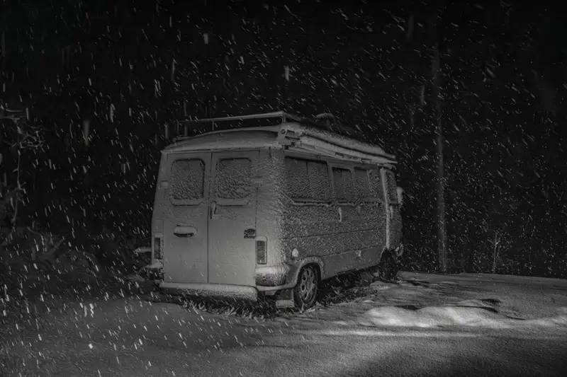Van parked on a street at night while snow falls.