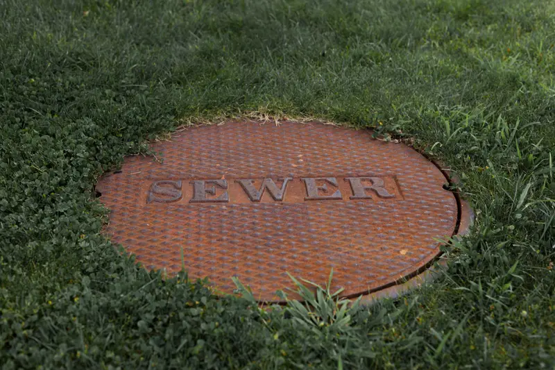 Cast-iron sewer access cover set in a grass lawn.