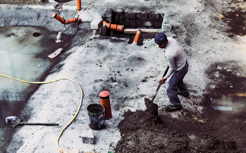 Worker digging a trench in snow with new pipe stubs in place.