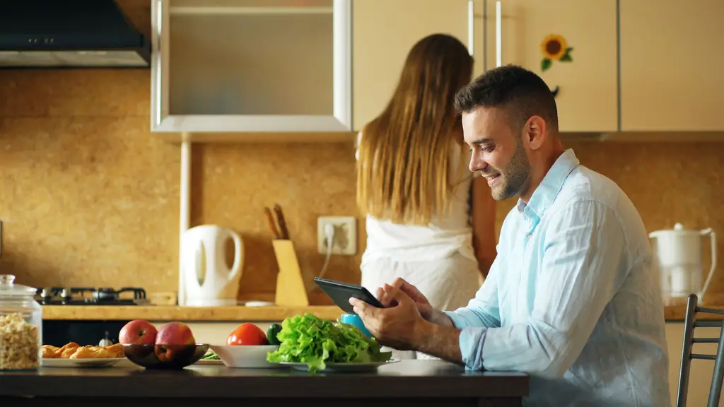 Man reviewing something on a tablet at a kitchen table.