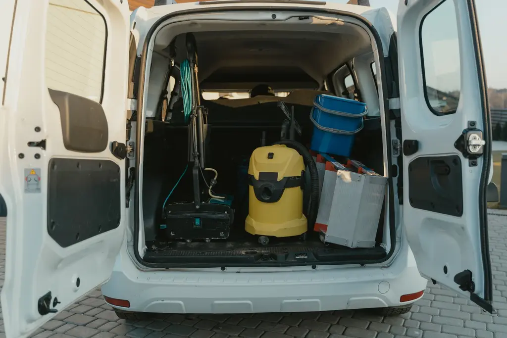 Open back of a white service van with tools and a wet-vac.